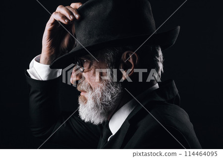 An old male actor playing an English spy role, hiding behind fedora hat. 114464095