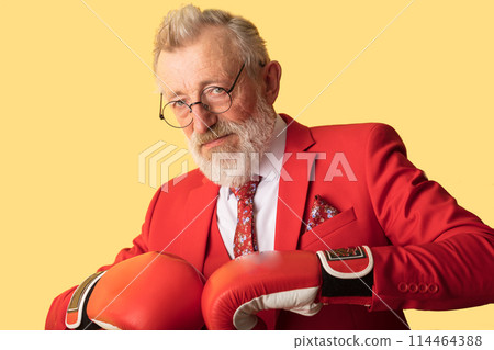 Senior business man in red suit and red boxing gloves standing in defence pose 114464388