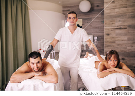 handsome talented masseur standing between a woman and a man handsome talented masseur standing between a woman and a man 114464539