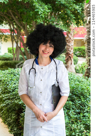 Experienced beautiful female doctor with lush hair on the territory of the clinic 114465985