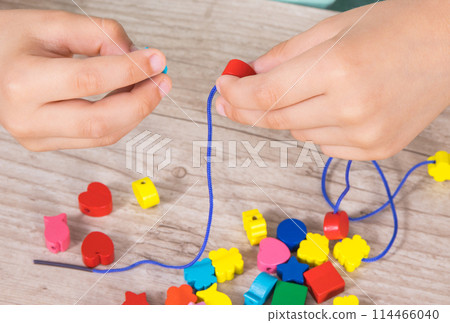Preschooler making bracelet from thread and colored beads. Development of kids motor skills 114466040