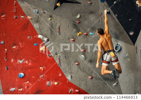 Young man climbing on artificial rock, hanging on safety ropes 114466913