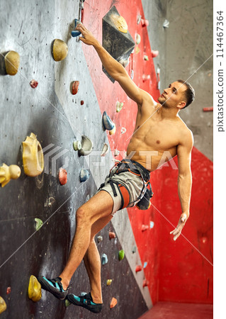 Man climber on artificial climbing wall in bouldering gym 114467364
