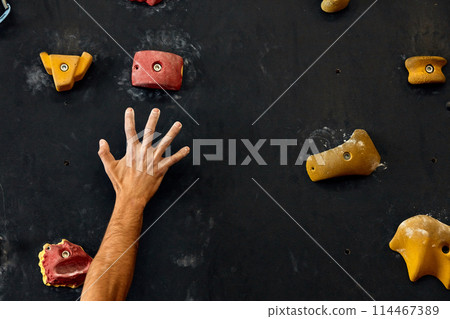 Macro shot of climbers hands gripping colourful handholds during indoor workout 114467389