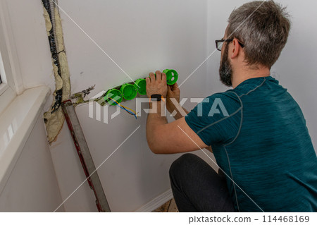 a man mounts wall sockets on plaster 114468169