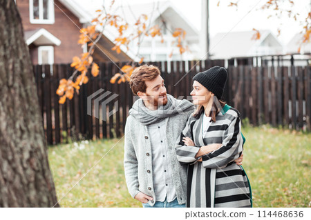 Happy young couple sitting outdoor, in front of their new home in autumn day Happy young couple sitting outdoor, in front of their new home in autumn day 114468636