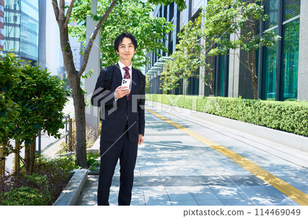 A businessman in a suit carrying a backpack operating a smartphone A businessman in a suit carrying a backpack operating a smartphone 114469049