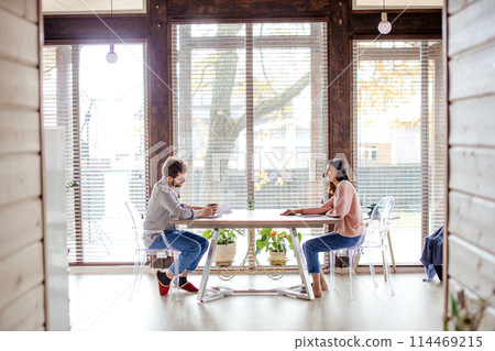 Couple sharing ideas, sitting opposite near big window. 114469215