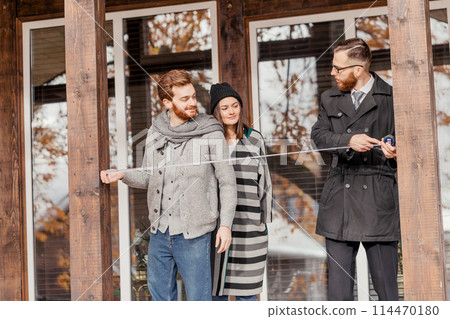 Real estate broker and clients standing next to house 114470180