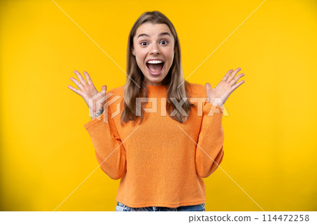 Happy emotions concept. Positive and beautiful young woman laughs poisitively looks aside with carefree face expression wears casual orange sweater isolated over yellow studio background. 114472258