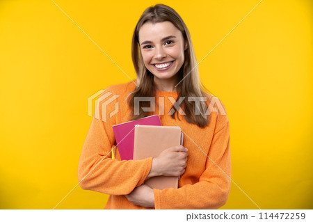 Happy emotions concept. Positive and beautiful young woman laughs poisitively looks aside with carefree face expression wears casual orange sweater isolated over yellow studio background. Happy emotions concept. Positive and beautiful young woman laughs poisitively looks aside with carefree face expression wears casual orange sweater isolated over yellow studio background. 114472259