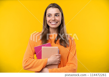 Happy emotions concept. Positive and beautiful young woman laughs poisitively looks aside with carefree face expression wears casual orange sweater isolated over yellow studio background. 114472261