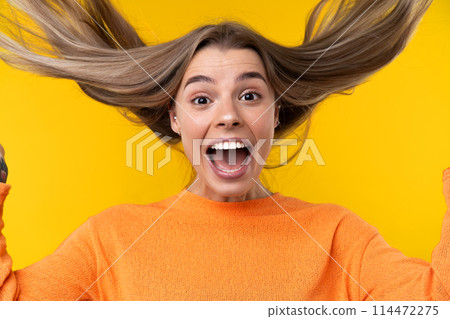 Happy emotions concept. Positive and beautiful young woman laughs poisitively looks aside with carefree face expression wears casual orange sweater isolated over yellow studio background. 114472275