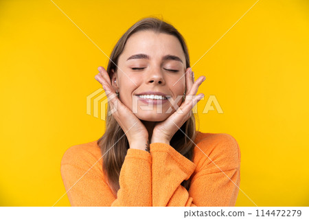 Happy emotions concept. Positive and beautiful young woman laughs poisitively looks aside with carefree face expression wears casual orange sweater isolated over yellow studio background. Happy emotions concept. Positive and beautiful young woman laughs poisitively looks aside with carefree face expression wears casual orange sweater isolated over yellow studio background. 114472279