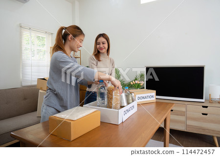 Happy young woman volunteer collecting, sorting food for needy people, team working together on donation project in charitable at home 114472457