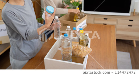 Group of volunteer woman working in home. Happy volunteer looking at food donation box separating donations stuffs Group of volunteer woman working in home. Happy volunteer looking at food donation box separating donations stuffs 114472472