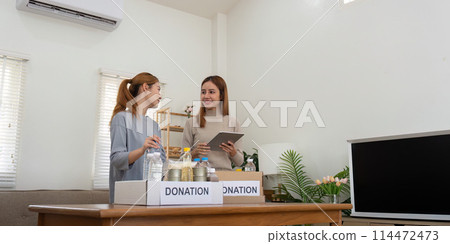 Happy young woman volunteer collecting, sorting food for needy people, team working together on donation project in charitable at home Happy young woman volunteer collecting, sorting food for needy people, team working together on donation project in charitable at home 114472473