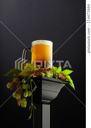 Mug of beer with green hops and wheat ears on a black background. 114472664
