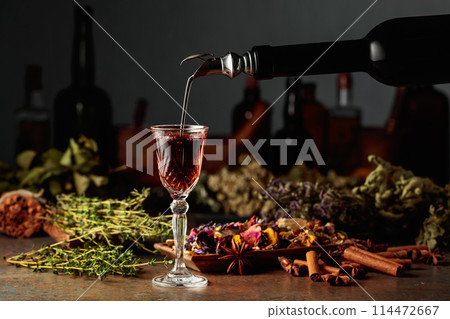 Brown herbal liquor or balm is poured from a vintage bottle into a glass. 114472667