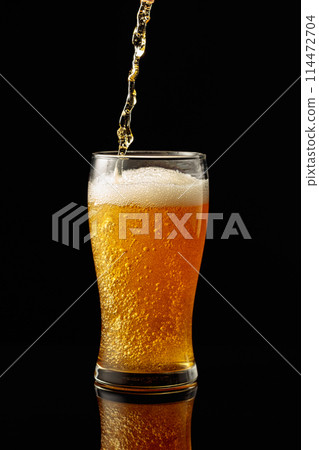 Pouring beer into a glass on a black reflective background. Pouring beer into a glass on a black reflective background. 114472704