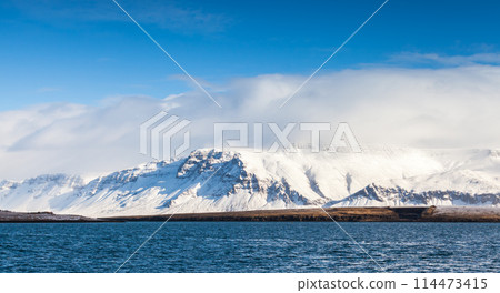 Coastal Icelandic landscape with snowy mountains under dramatic blue sky Coastal Icelandic landscape with snowy mountains under dramatic blue sky 114473415