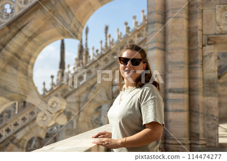 Beautiful 30s woman in sunglasses posing on Roof of Milan Cathedral Duomo di Milano, Italy. Traveling Europe in summer. Attractive blonde female is exploring city. Top tourist attraction. 114474277