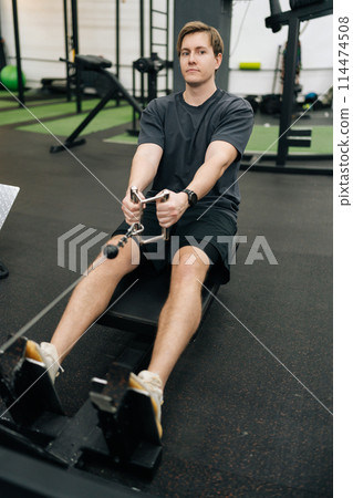 Vertical portrait of beginner sportsman doing exercises on fitness machine in gym. Motivated sporty male with pull cable or equipment for health goals at sport club. Concept of healthy sports life. Vertical portrait of beginner sportsman doing exercises on fitness machine in gym. Motivated sporty male with pull cable or equipment for health goals at sport club. Concept of healthy sports life. 114474508