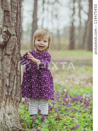 blond baby in a colored dress running in a forest glade with flowers 114475450