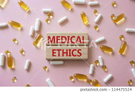 Medical Ethics symbol. Concept word Medical Ethics on wooden blocks. Beautiful pink background with pills. Medicine and Medical Ethics concept. Copy space 114475524
