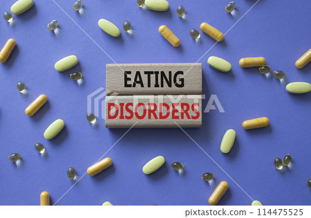 Eating Disorders symbol. Concept word. Eating Disorders on wooden blocks. Beautiful purple background with pills. Medicine and Eating Disorders concept. Copy space Eating Disorders symbol. Concept word. Eating Disorders on wooden blocks. Beautiful purple background with pills. Medicine and Eating Disorders concept. Copy space 114475525