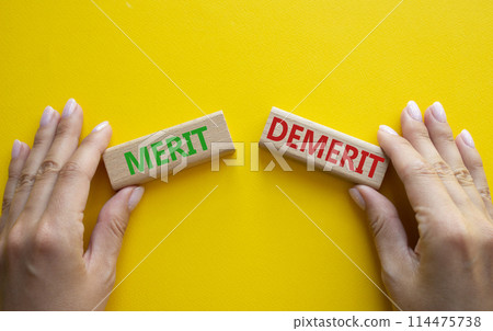 Merit or Demerit symbol. Concept word Merit or Demerit on wooden blocks. Businessman hand. Beautiful yellow background. Business and Merit or Demerit concept. Copy space Merit or Demerit symbol. Concept word Merit or Demerit on wooden blocks. Businessman hand. Beautiful yellow background. Business and Merit or Demerit concept. Copy space 114475738