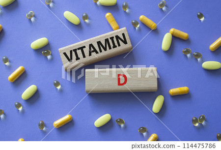 Vitamin D symbol. Concept word Vitamin D on wooden blocks. Beautiful purple background with pills. Medicine and Vitamin D concept. Copy space 114475786