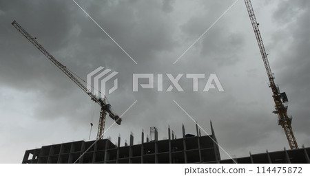 The building cranes rotates from the wind. Strong wind. Crane on construction site. Bad weather with cloudy sky against the cranes. The building cranes rotates from the wind. Strong wind. Crane on construction site. Bad weather with cloudy sky against the cranes. 114475872