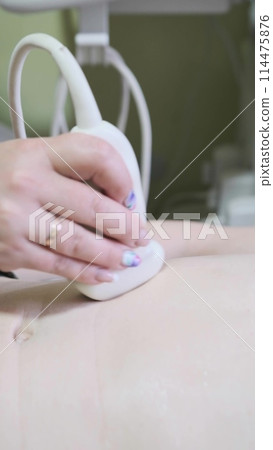 Abdominal ultrasound. Close-up of doctor's hand with ultrasound probe. Ultrasound diagnosis of the stomach on the abdominal cavity of a man in the clinic, close-up view vertical Abdominal ultrasound. Close-up of doctor's hand with ultrasound probe. Ultrasound diagnosis of the stomach on the abdominal cavity of a man in the clinic, close-up view vertical 114475876