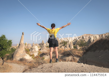 Woman tourist standing back with raised hands on turkish mountains background in Cappadocia 114475914