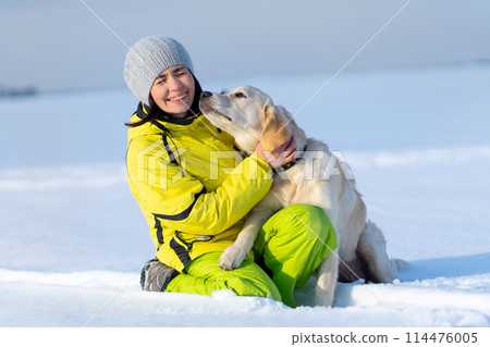 Cute young retriever dog kissing laughing woman on snowy field 114476005