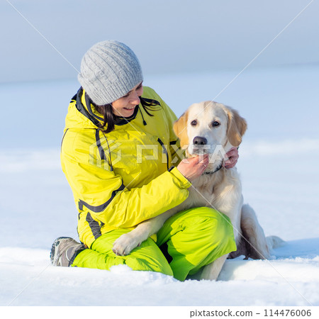 Happy girl with cute young golden retriever dog sitting in snow Happy girl with cute young golden retriever dog sitting in snow 114476006