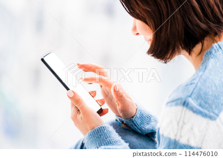 Woman using smartphone in light room Woman using smartphone in light room 114476010