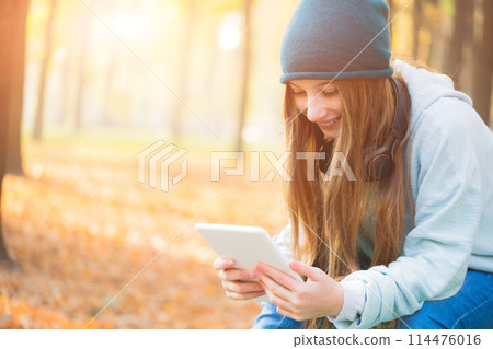 Smiling girl reading on tablet sitting in park 114476016