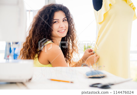 Smiling tailor pinning parts of dress in workshop Smiling tailor pinning parts of dress in workshop 114476024