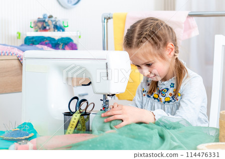 Little girl using sewing machine to make crafts in the workshop 114476331
