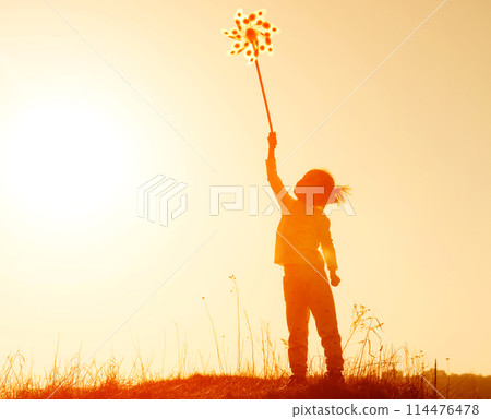 Little girl playing with wind toy or pinwheel against the sky at sunset. Happy girl silhouette Little girl playing with wind toy or pinwheel against the sky at sunset. Happy girl silhouette 114476478