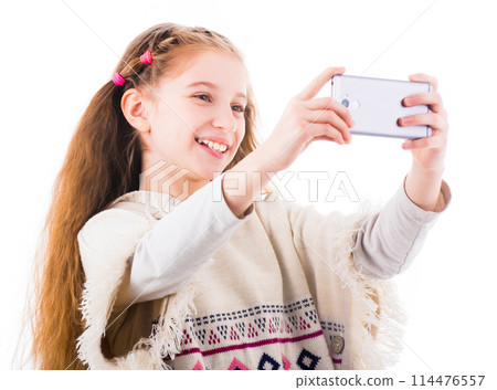 Smilling young little girl makes selfie with her mobile phone isolated on white background Smilling young little girl makes selfie with her mobile phone isolated on white background 114476557