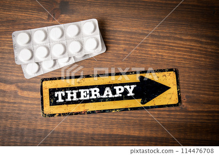 Therapy. Direction arrow with text and pills on wooden texture table 114476708