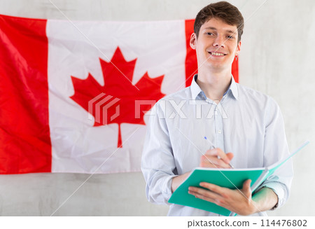 Young guy makes notes against background of Canada flag Young guy makes notes against background of Canada flag 114476802