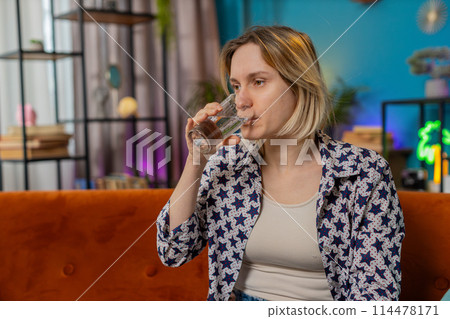 Satisfied Caucasian woman sitting at home on couch leading healthy lifestyle drinking pure water 114478171