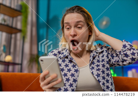 Surprised excited young woman winner holding smartphone reading good news amazed by online game win Surprised excited young woman winner holding smartphone reading good news amazed by online game win 114478219