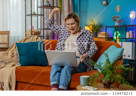 Happy woman using laptop receive good news shocked by victory celebrate lottery jackpot win at home 114478231