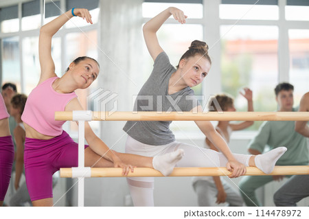 Teen ballet students prepare for classes, near ballet bare stretch legs under man teacher guidance 114478972