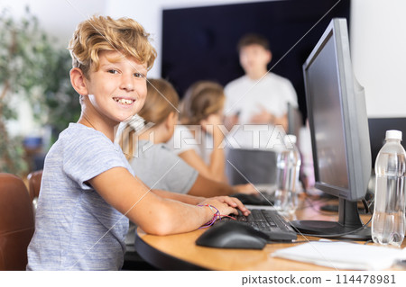 Smiling preteen boy sitting at computer table in training room Smiling preteen boy sitting at computer table in training room 114478981